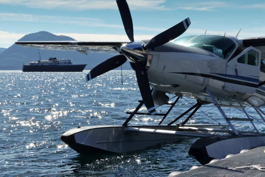 A float plane on the water with a ferry in the background.