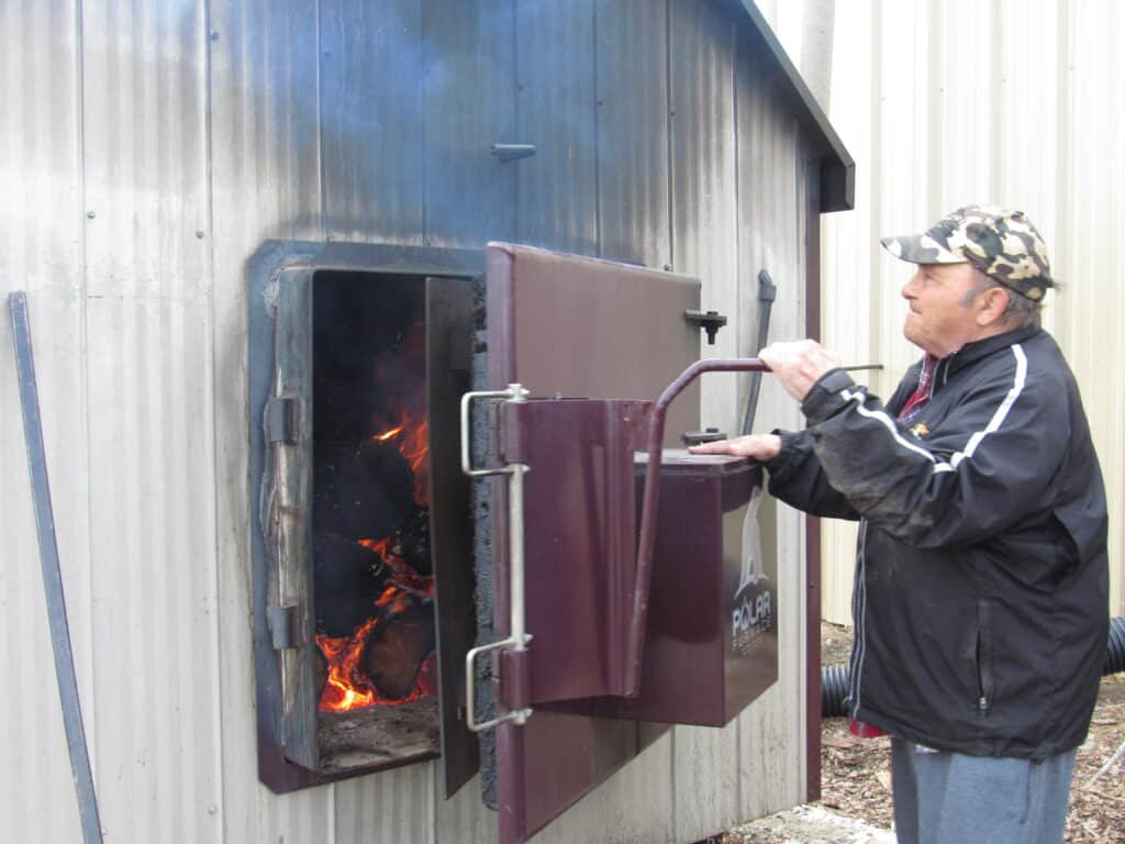 A man closing the door of a furnace burning logs.