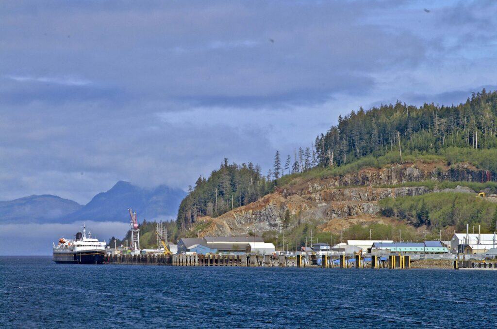 A large boat is docked at the dock in front of a mountain.