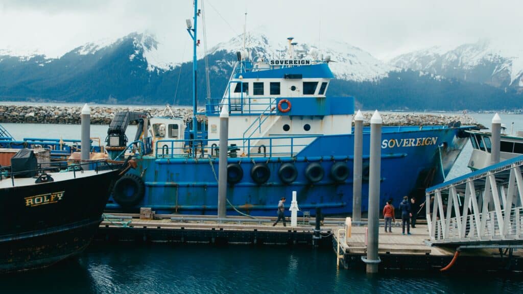 A blue boat docked at a dock with a mountain in the background.